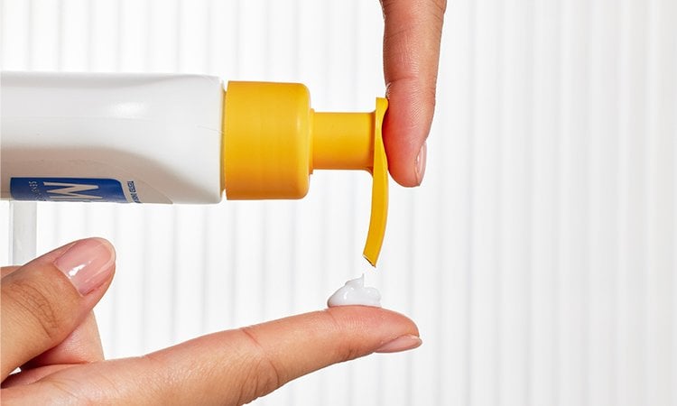 Eine Person gibt mit einem Pumpspender etwas Niacinamide Bright Bodylotion auf einen Finger.